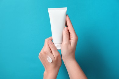 Photo of Woman with tube of hand cream on light blue background, closeup