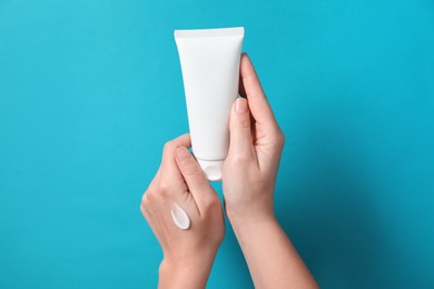 Woman with tube of hand cream on light blue background, closeup