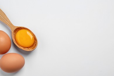 Photo of Raw chicken eggs and spoon with yolk on white background, flat lay. Space for text