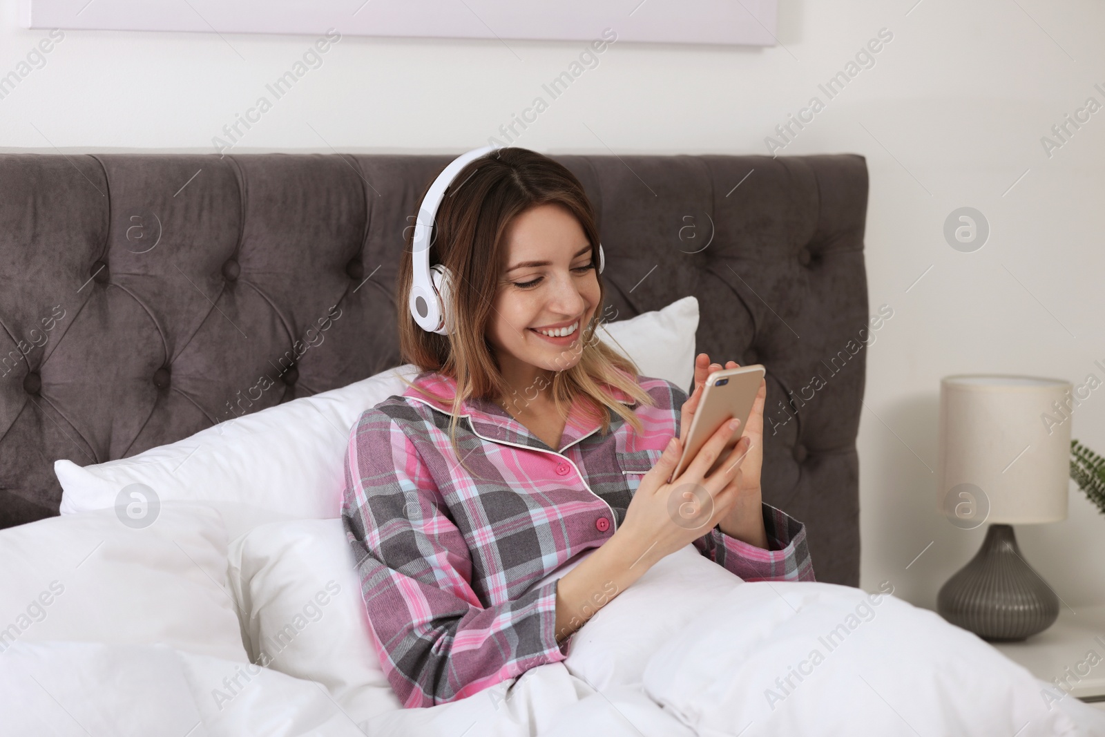 Photo of Young woman with headphones and mobile device enjoying music in bed