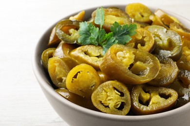 Photo of Bowl with slices of pickled green jalapeno peppers on white table, closeup