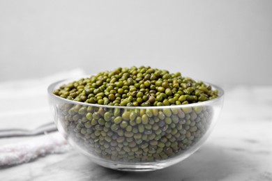 Photo of Glass bowl with green mung beans on white marble table, closeup