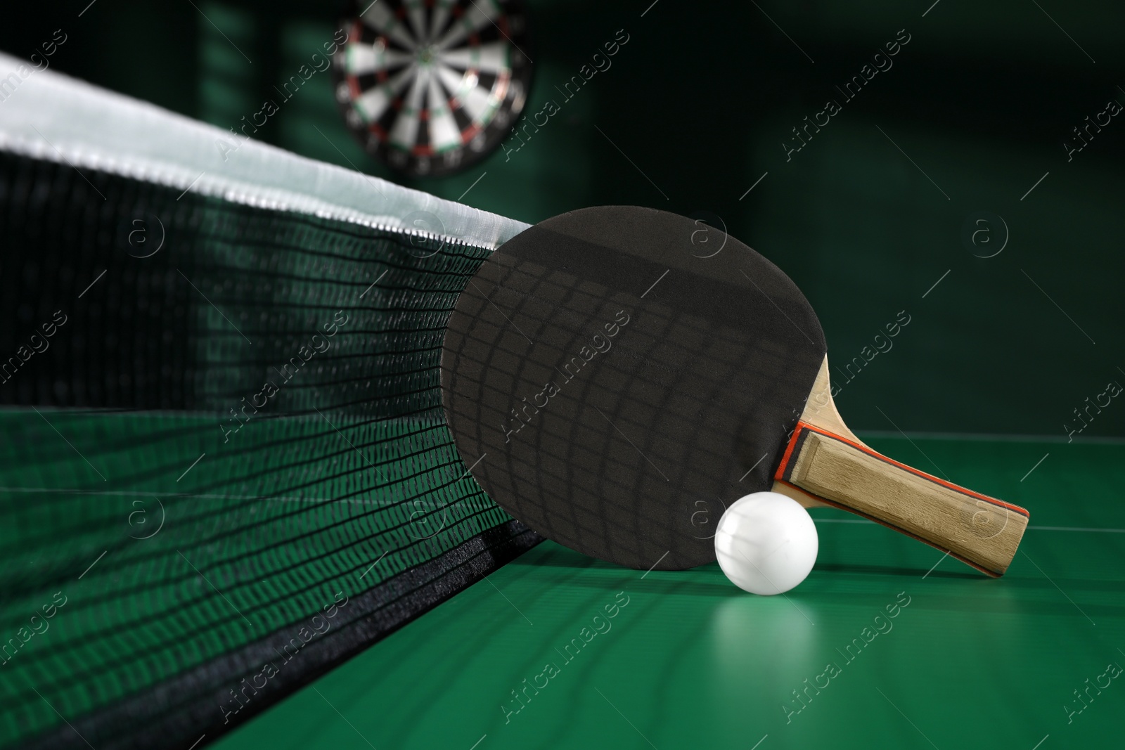 Photo of Black racket and ball on green ping pong table indoors