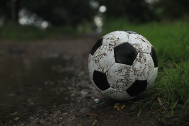 Dirty leather soccer ball near puddle outdoors, space for text