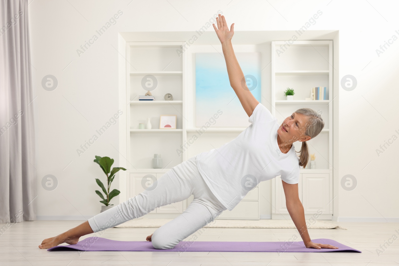 Photo of Happy senior woman practicing yoga on mat at home