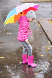 Little girl with umbrella splashing in puddle on rainy day. Autumn walk