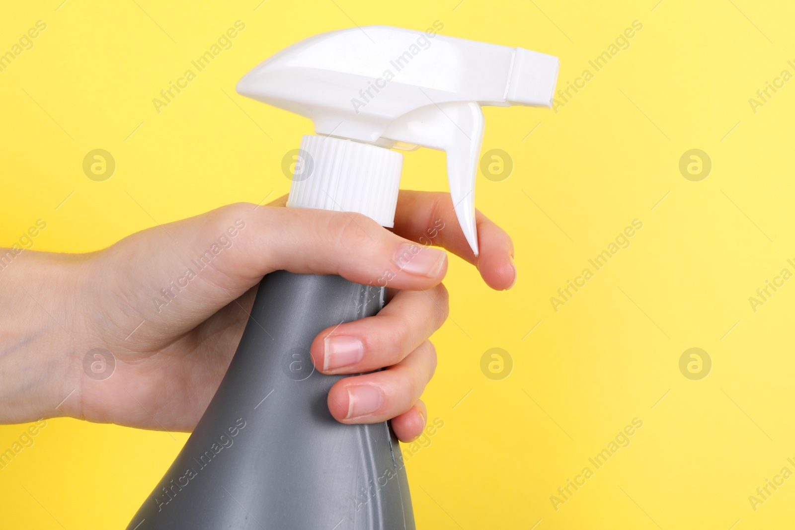 Photo of Woman holding plastic spray bottle on yellow background, closeup. Space for text