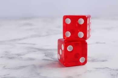 Photo of Two red game dices on white marble table, closeup. Space for text