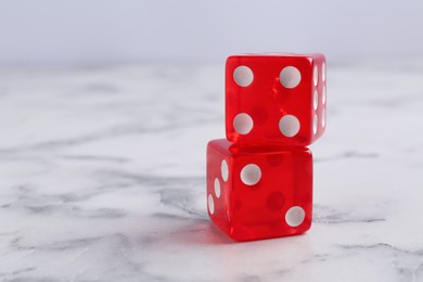 Two red game dices on white marble table, closeup. Space for text