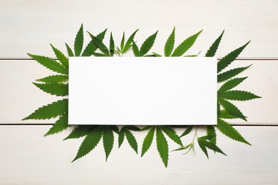 Photo of Fresh green hemp leaves and blank card on white wooden table, top view. Space for text