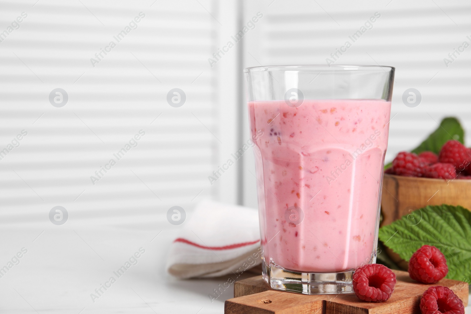 Photo of Tasty raspberry smoothie in glass on white table, space for text