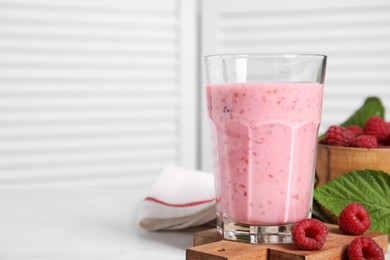 Tasty raspberry smoothie in glass on white table, space for text