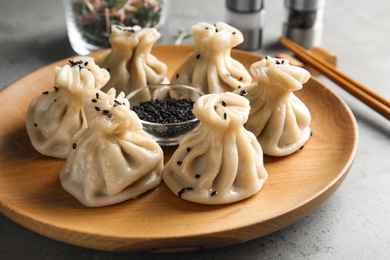 Photo of Wooden plate with tasty baozi dumplings and sesame seeds on table