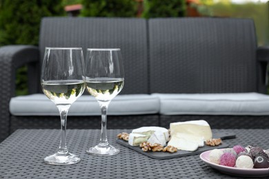Glasses of wine and different snacks on rattan table on outdoor terrace