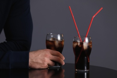 Photo of Man with glass of iced cola at table against grey background, closeup