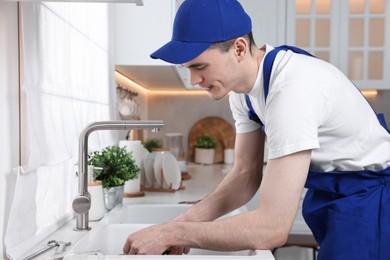 Photo of Young plumber wearing uniform repairing sink in kitchen