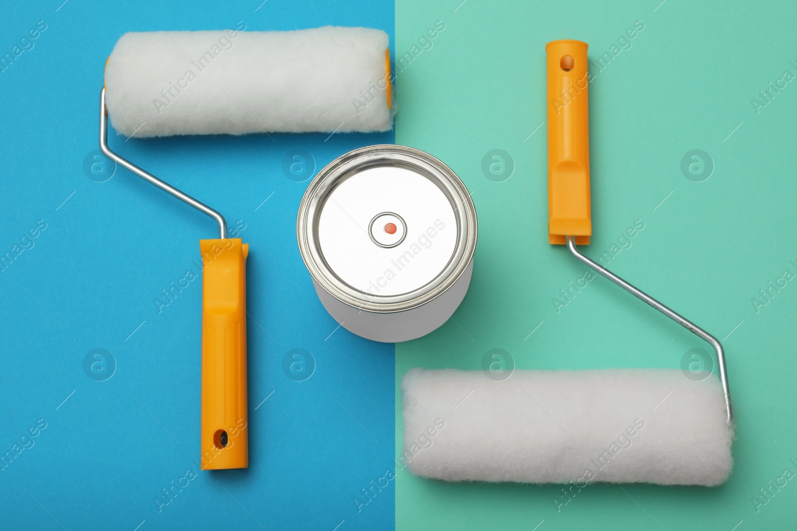 Photo of Can of orange paint and roller brushes on color background, flat lay