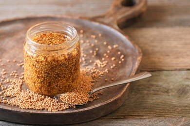 Photo of Jar and spoon of whole grain mustard on wooden table, closeup. Space for text