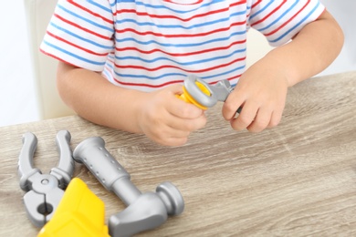 Photo of Little boy playing with toy construction tools at wooden table, closeup