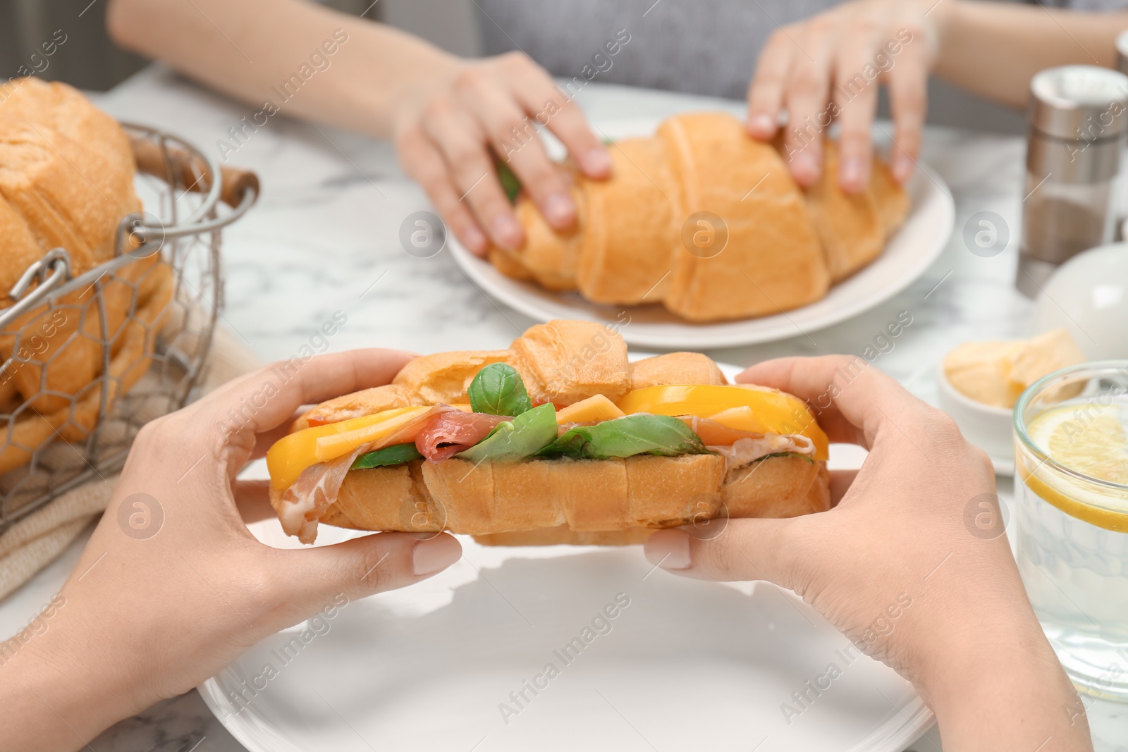 Photo of Woman holding tasty croissant sandwich over plate at table