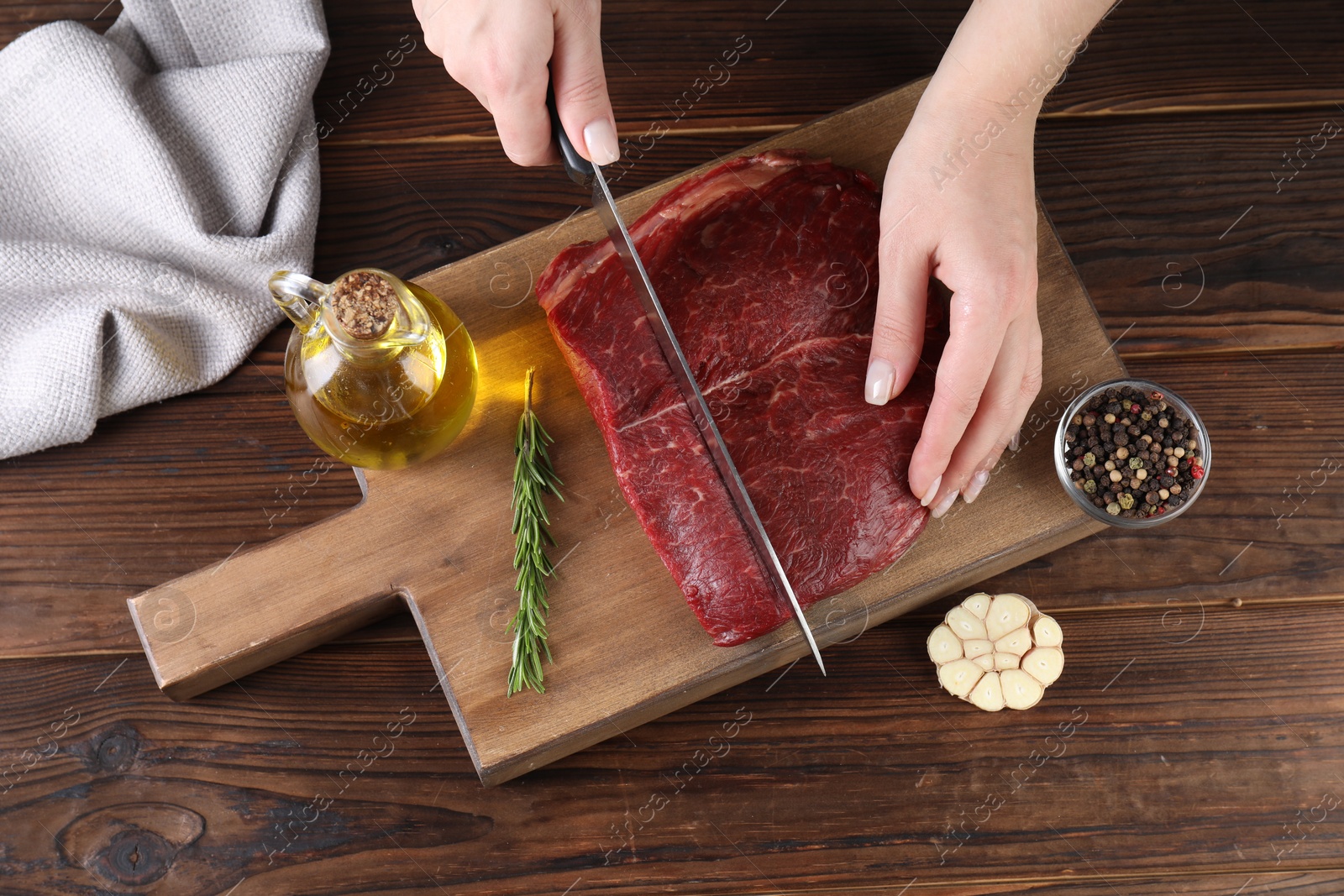 Photo of Woman cutting fresh raw beef steak at wooden table, top view