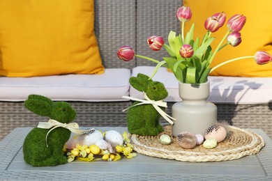 Photo of Terrace with Easter decorations. Bouquet of tulips in vase, bunny figures and decorated eggs on table outdoors