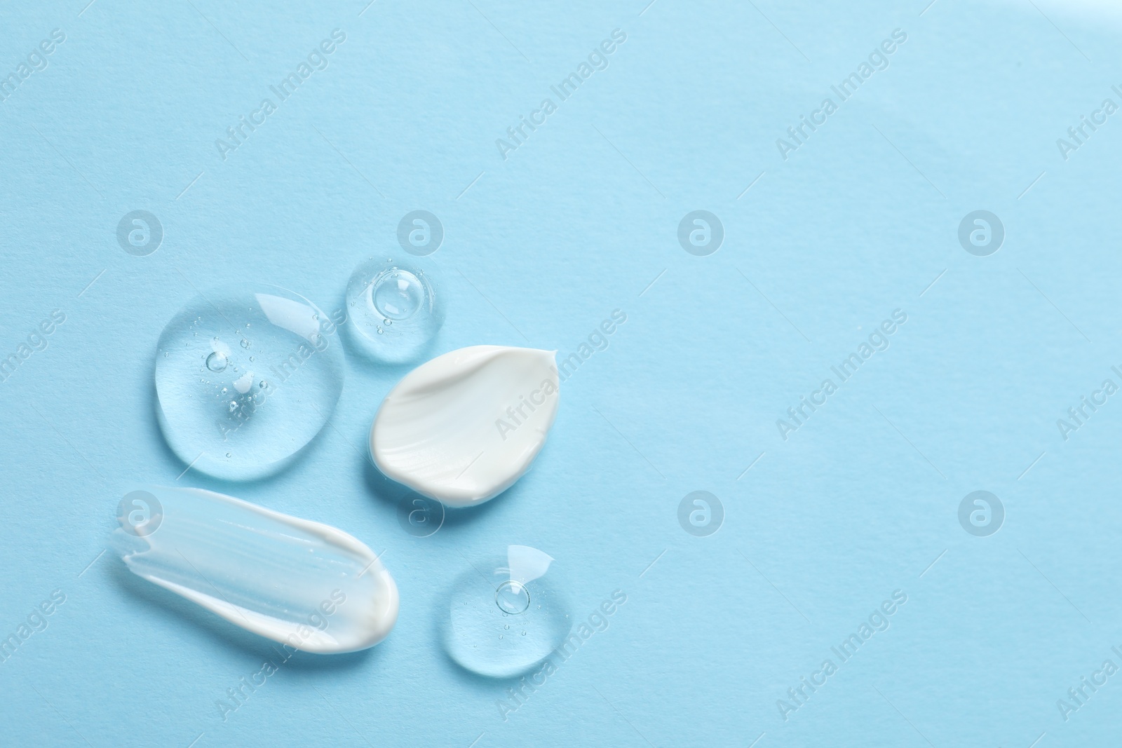 Photo of Samples of transparent gel and white cream on light blue background, flat lay. Space for text