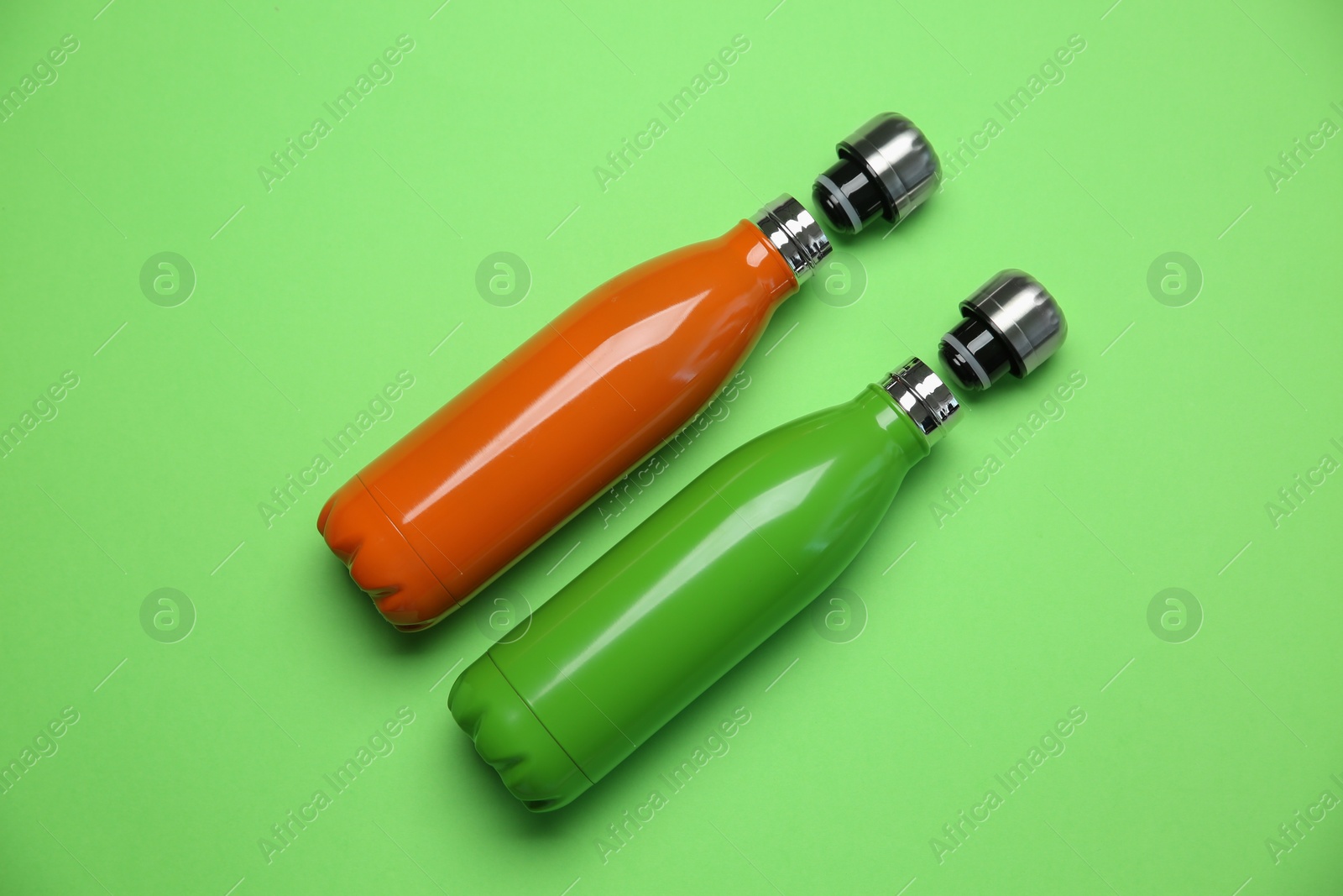 Photo of Different thermo bottles on green background, flat lay