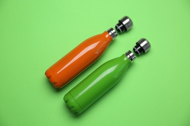 Photo of Different thermo bottles on green background, flat lay