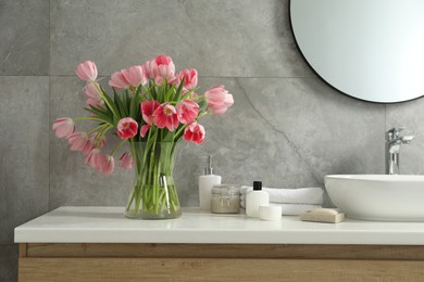 Photo of Vase with beautiful pink tulips and toiletries near sink in bathroom