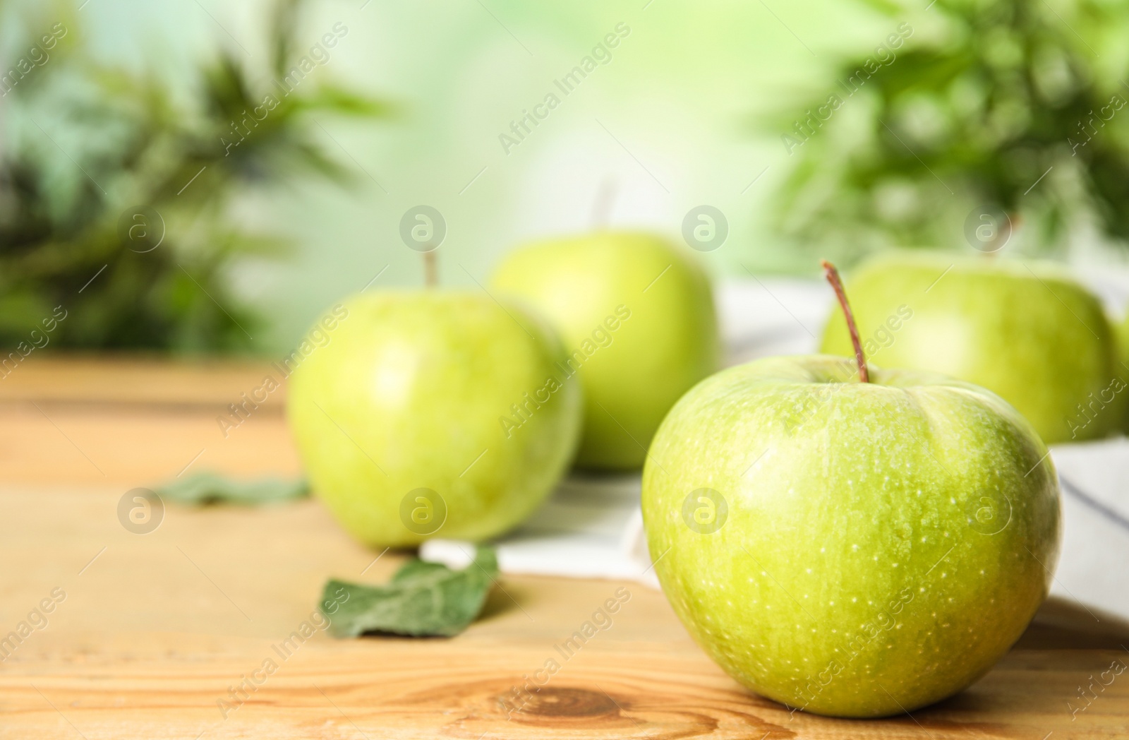 Photo of Fresh ripe green apples on wooden table against blurred background, space for text