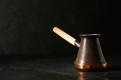 Photo of Beautiful copper turkish coffee pot with wooden handle on black table. Space for text