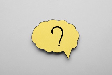 Paper speech bubble with question mark on light grey background, above view