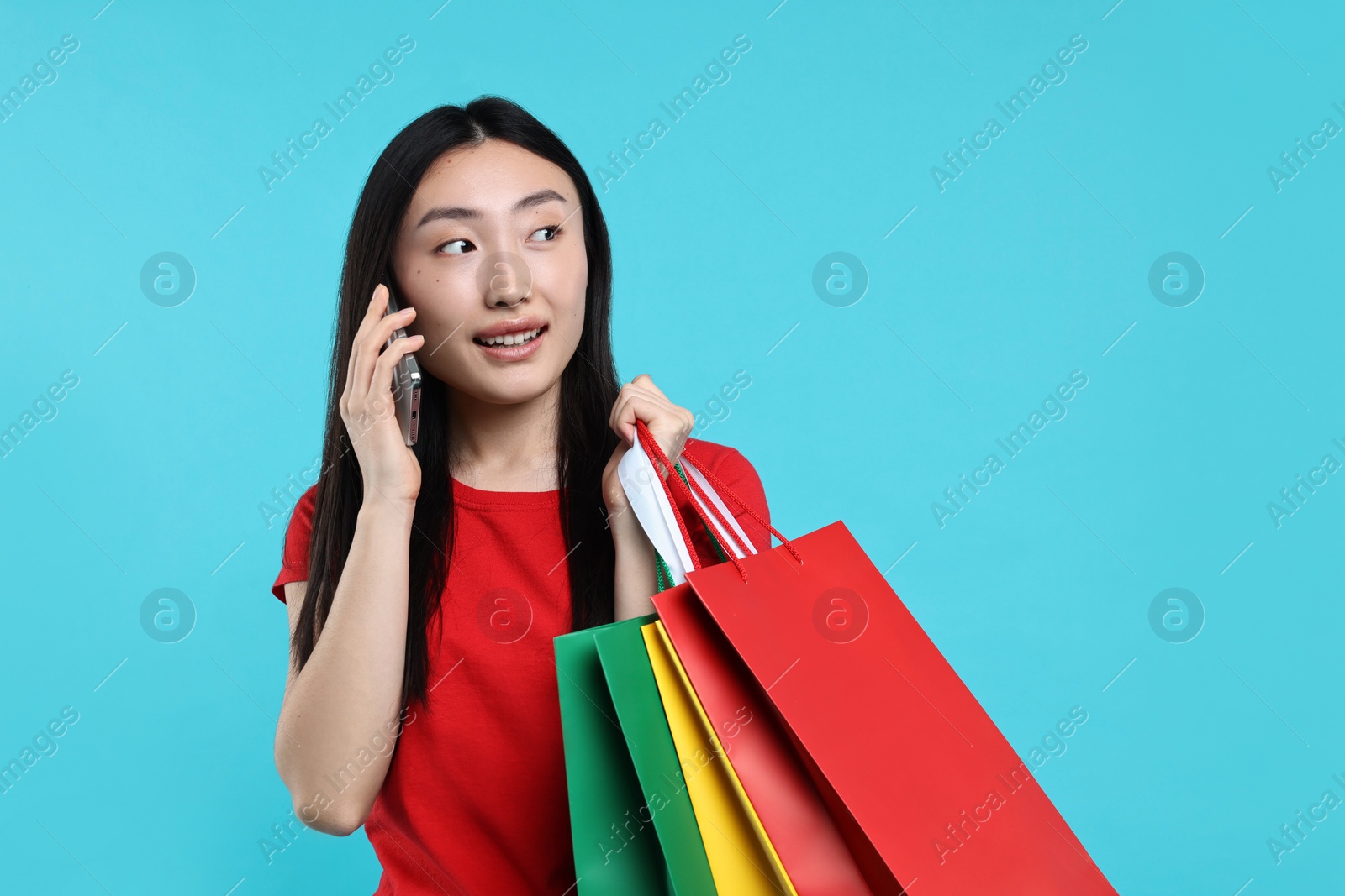 Photo of Smiling woman with shopping bags talking by smartphone on light blue background. Space for text