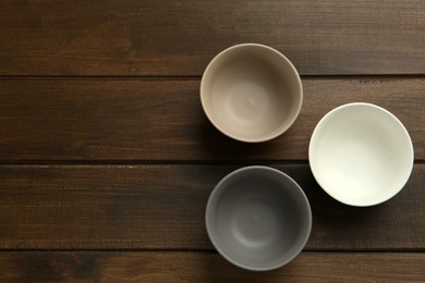 Photo of Stylish empty ceramic bowls on wooden table, flat lay and space for text. Cooking utensils