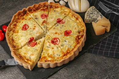 Photo of Taking piece of delicious homemade cheese quiche and ingredients on gray table