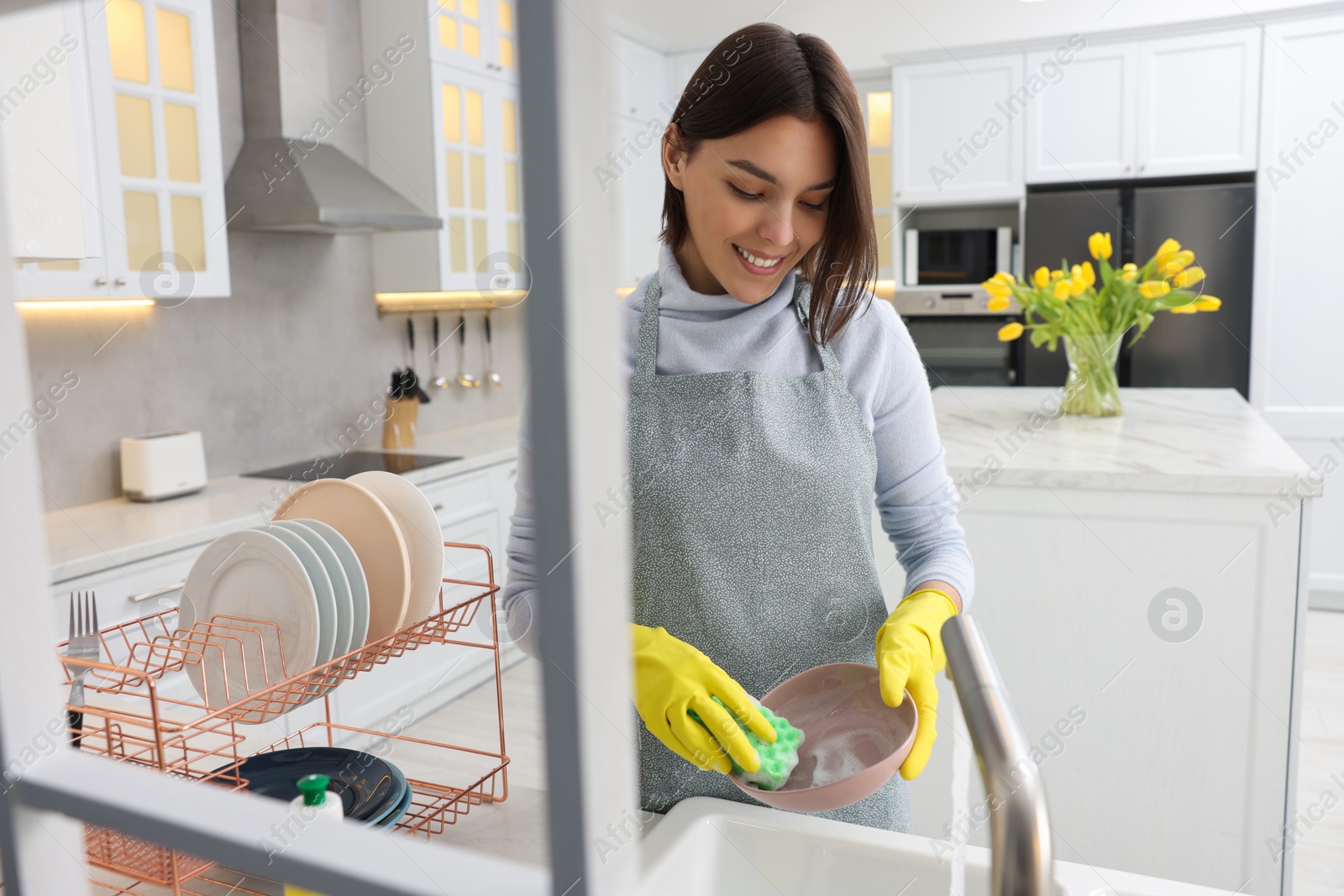 Photo of Happy young woman washing plate above sink in modern kitchen