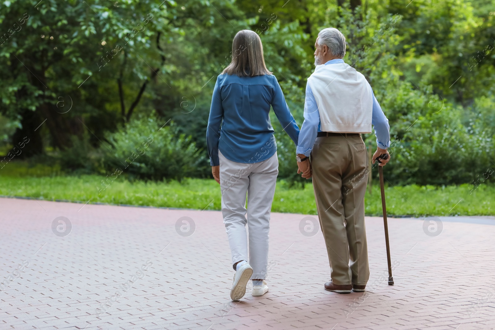 Photo of Senior man with walking cane and mature woman outdoors, back view. Space for text