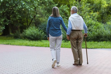 Photo of Senior man with walking cane and mature woman outdoors, back view. Space for text