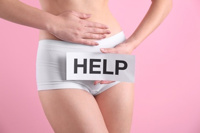 Photo of Young woman holding paper with word HELP near underwear on color background. Gynecology