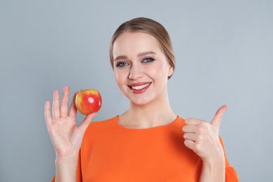 Photo of Young woman with apple on grey background. Vitamin rich food