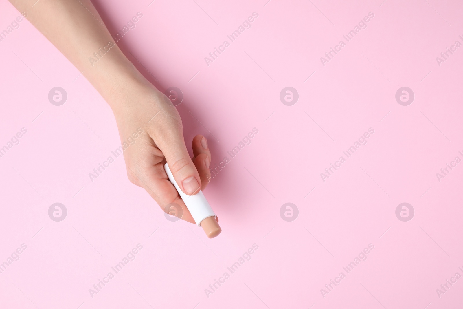 Photo of Woman holding hygienic lipstick on pink background, top view. Space for text