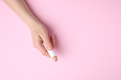 Photo of Woman holding hygienic lipstick on pink background, top view. Space for text