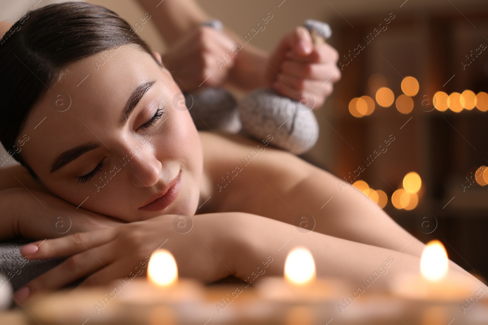 Photo of Spa therapy. Beautiful young woman lying on table during herbal bag massage in salon, closeup