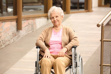 Happy senior woman in wheelchair near ramp outdoors