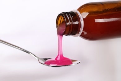 Photo of Pouring cough syrup into spoon on white background, closeup