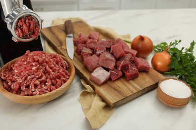 Electric meat grinder with beef and products on white marble table