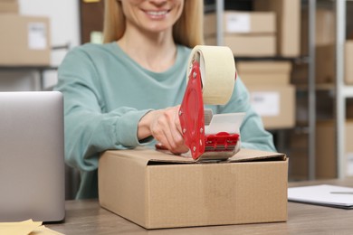 Seller taping parcel at table in office, closeup. Online store