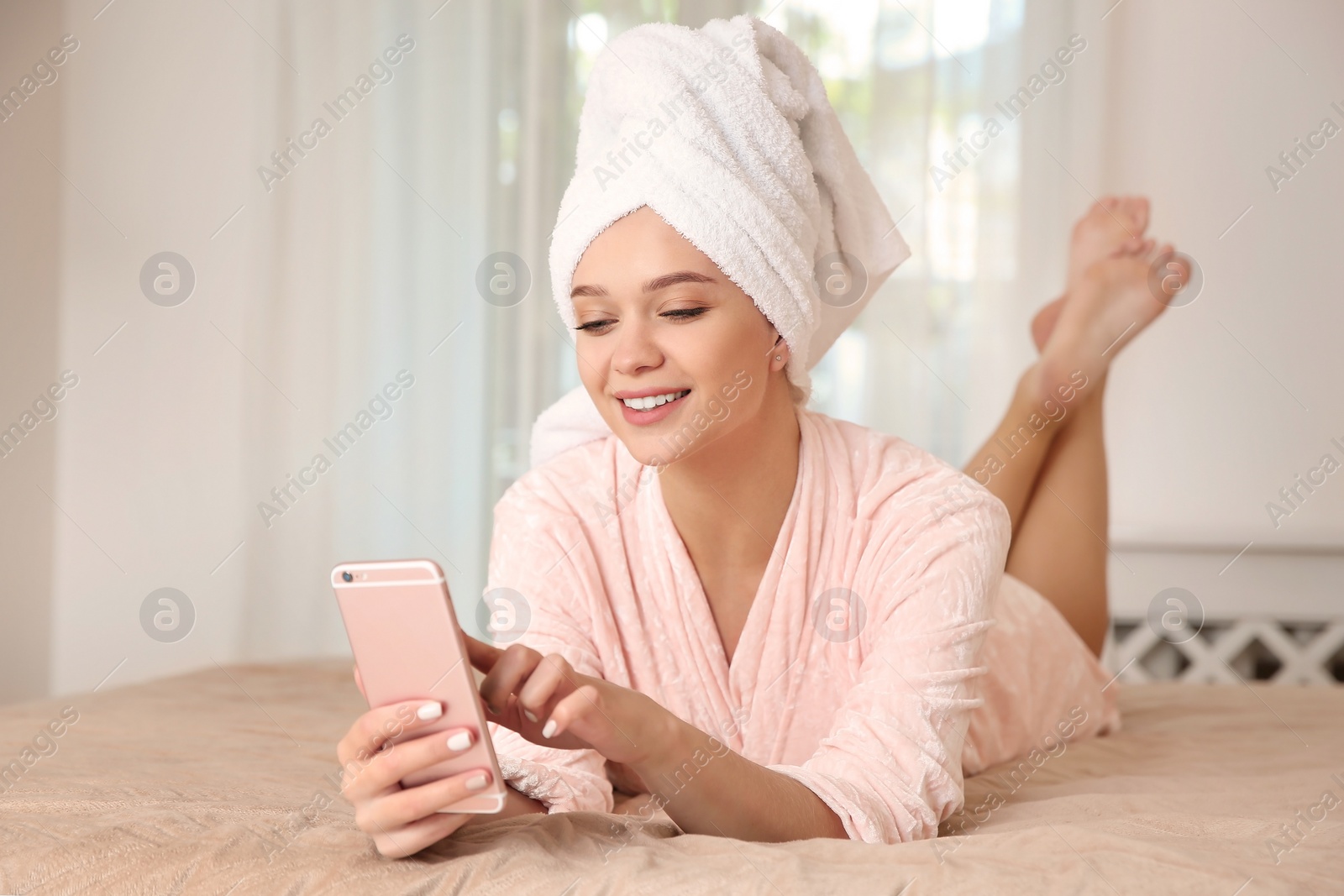 Photo of Beautiful woman with towel on head using phone in bedroom at home