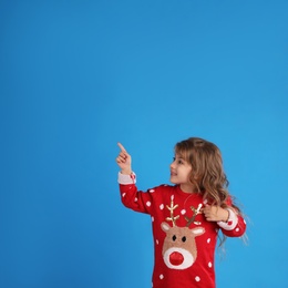 Cute little girl in red Christmas sweater pointing against blue background. Space for text